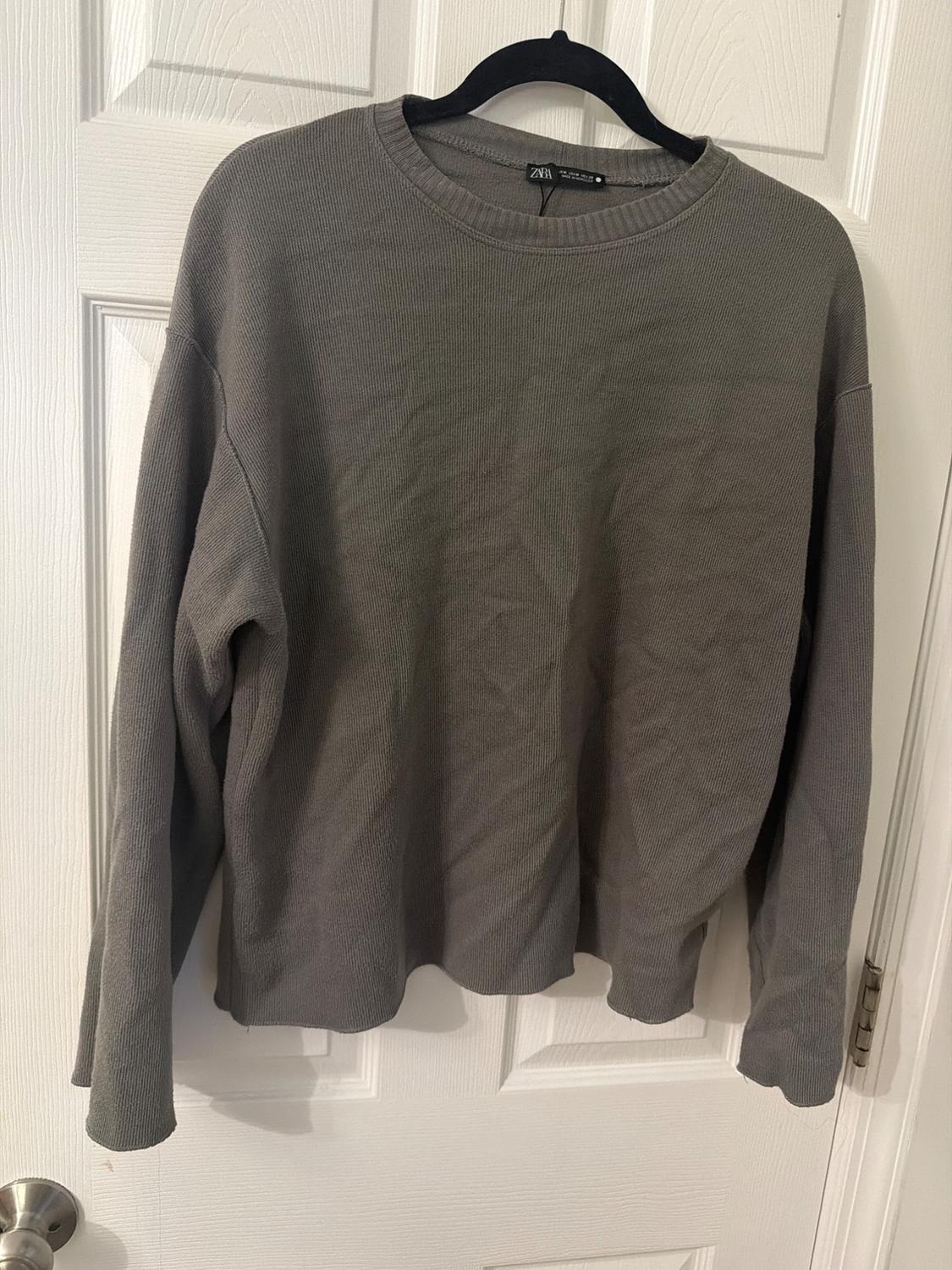 Gray sweater hanging on a black hanger over a white door. Label visible on the collar.
