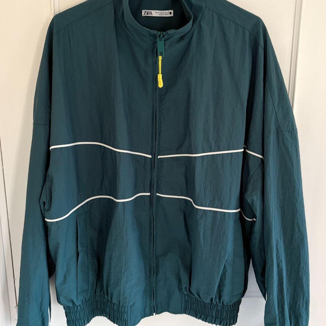 Green jacket with zip and horizontal white line details. Visible inner label with the ZARA brand.