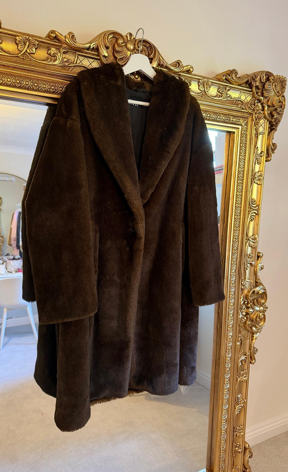 Brown faux fur coat hanging on an ornate gold mirror. Background with a light-coloured room and furniture.