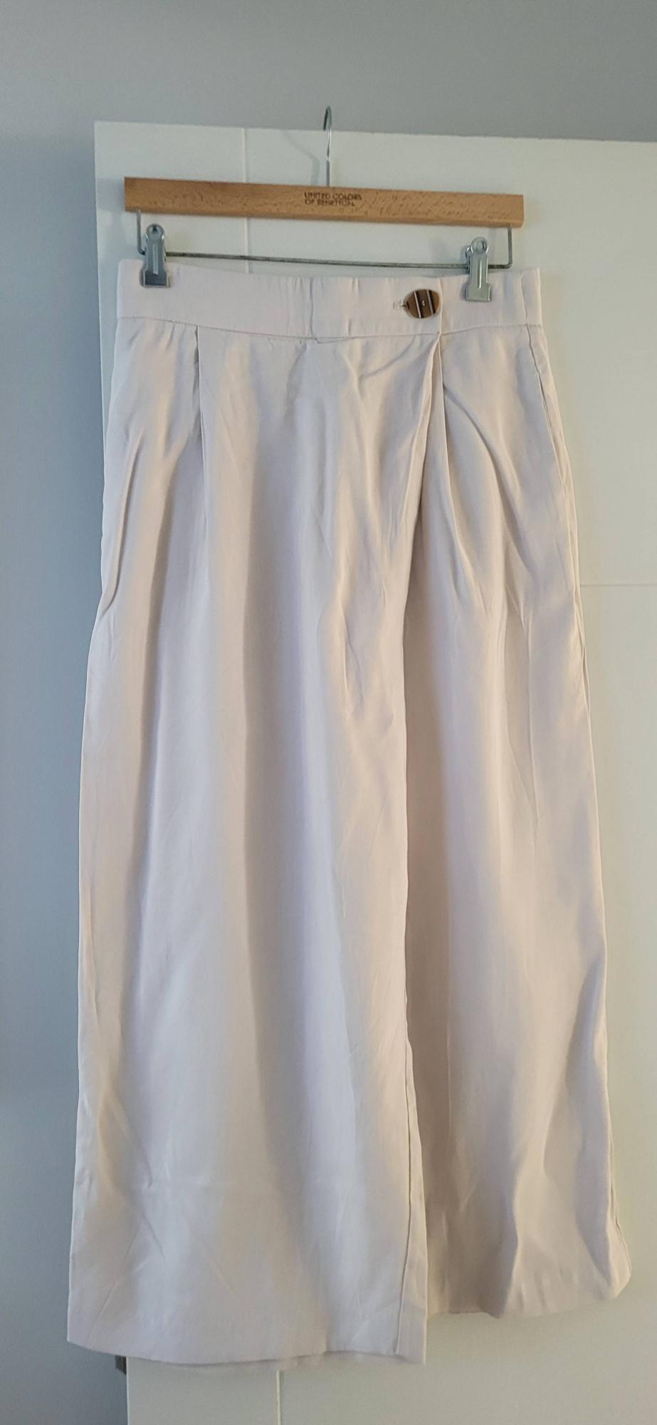 Beige skirt hanging on a wooden hanger with "United Colors of Benetton" text, white and light grey background.