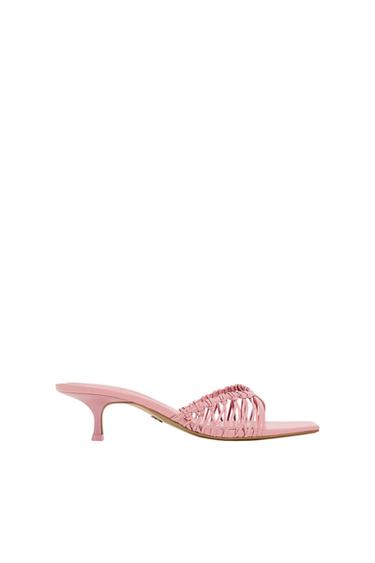 Pink sandal with a low heel and woven design on the upper, on a white background.