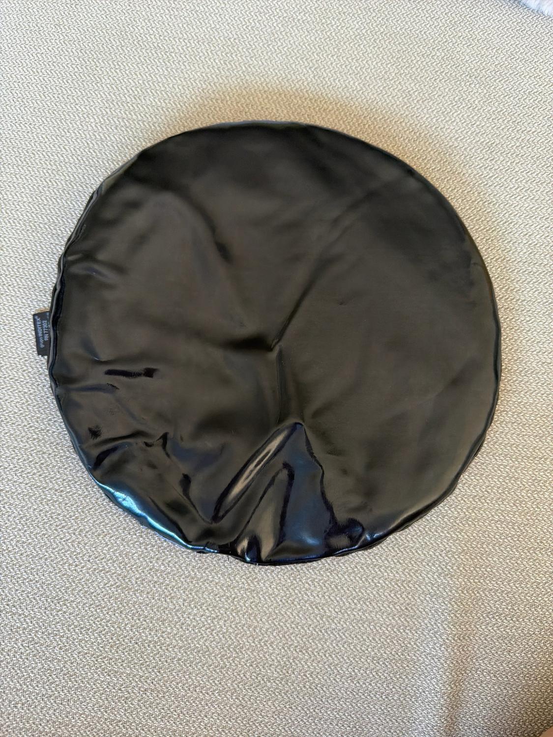 Glossy black round accessory with folds on a textured fabric background. Label with the text INDITEX group RN 77302.