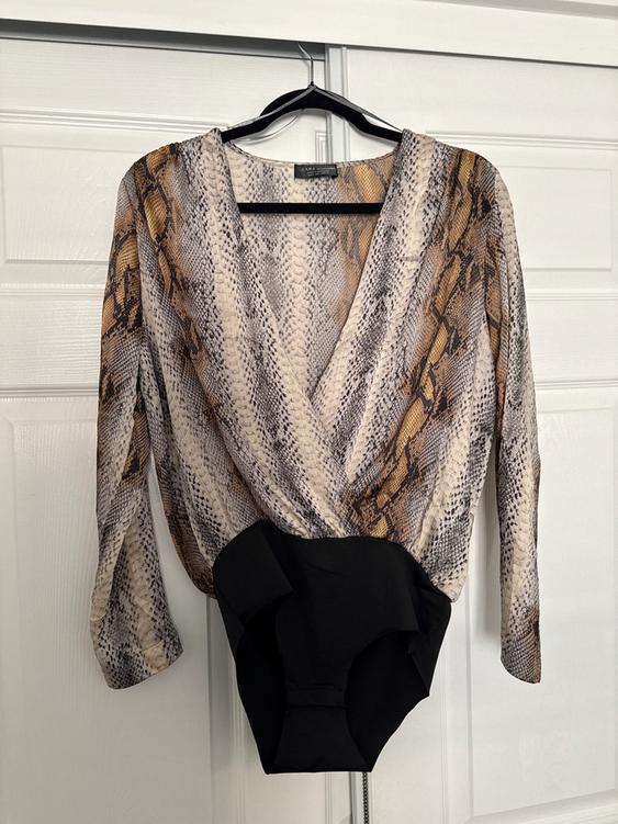 Long-sleeved bodysuit with snake print in brown and black tones, hanging on a black hanger in front of a white door.