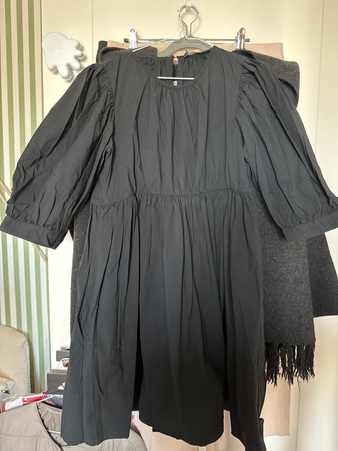Long-sleeved black dress hanging on a hanger over a grey coat. Background with a green and white striped wall.