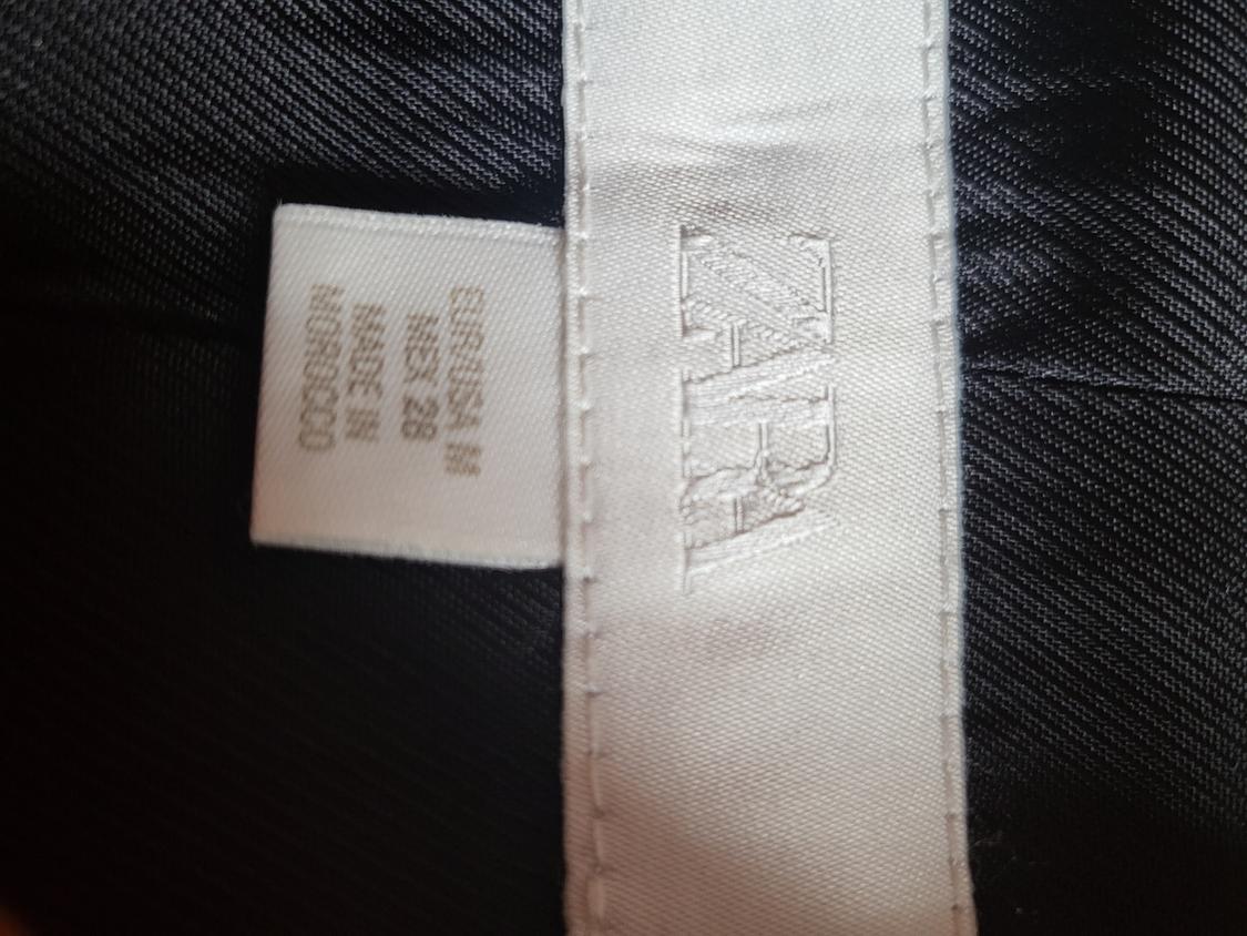 Close-up of a white label on black fabric with the text ZARA, EUR/USA M, MEX 28, MADE IN MOROCCO.