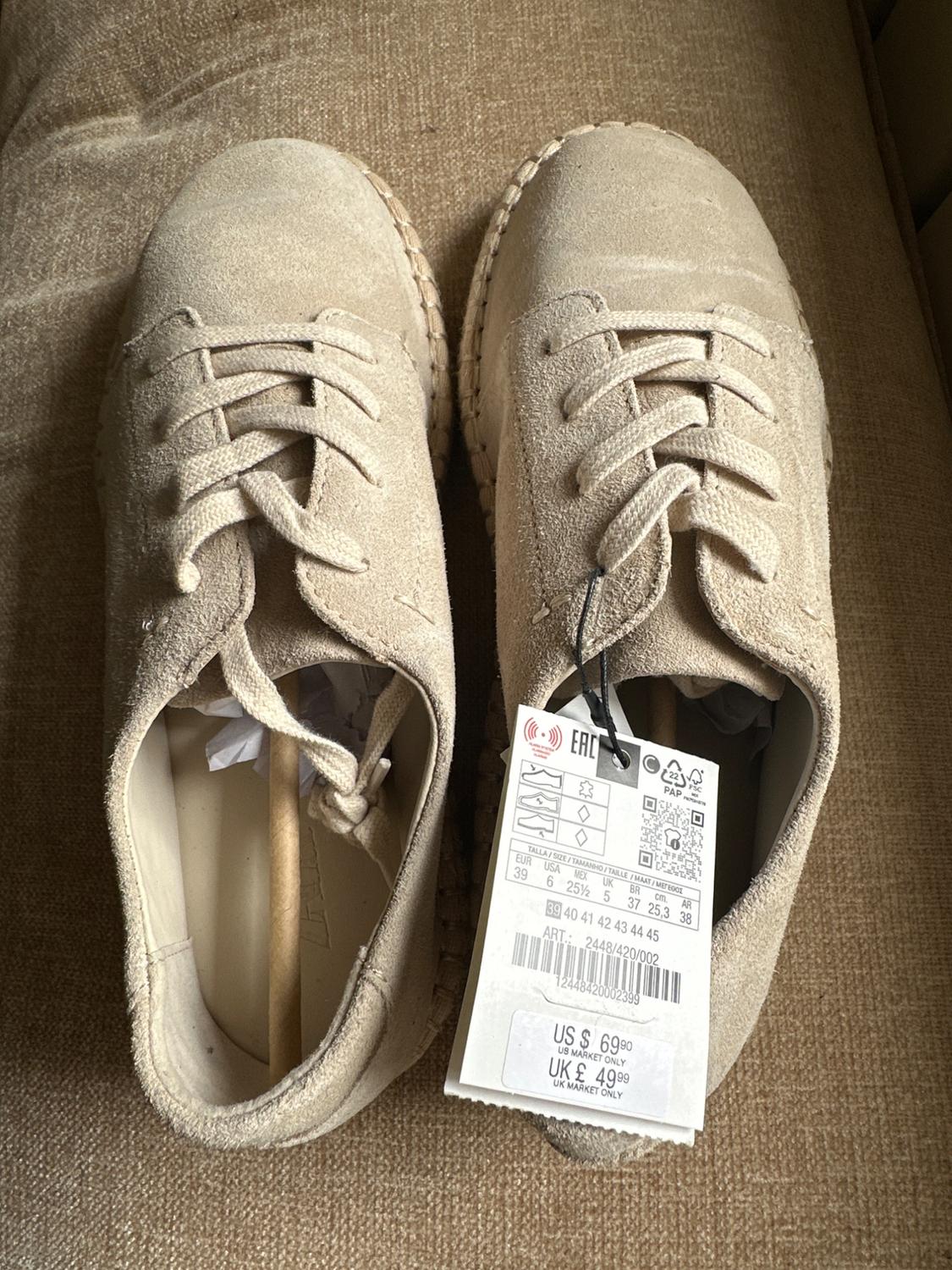 Zapatos de ante beige con cordones sobre tela. Texto: ART.: 2448/420/002 US $ 69.90 US MARKET ONLY UK £ 49.99 UK MARKET ONLY.