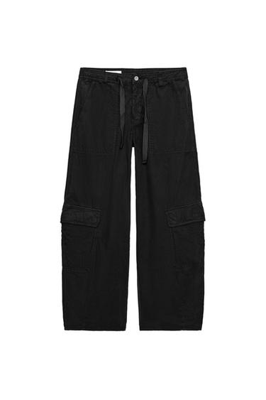 Front view of oversized black cargo pants with patch pockets on the front and leg, front zip and button closure.