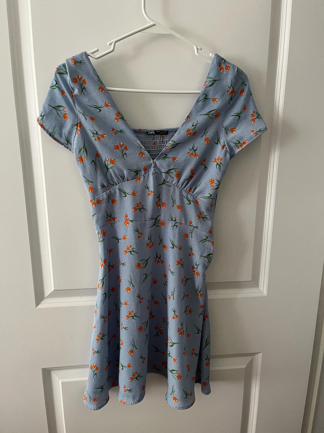 Light blue dress with an orange and green floral pattern, hanging on a white hanger over a white door.