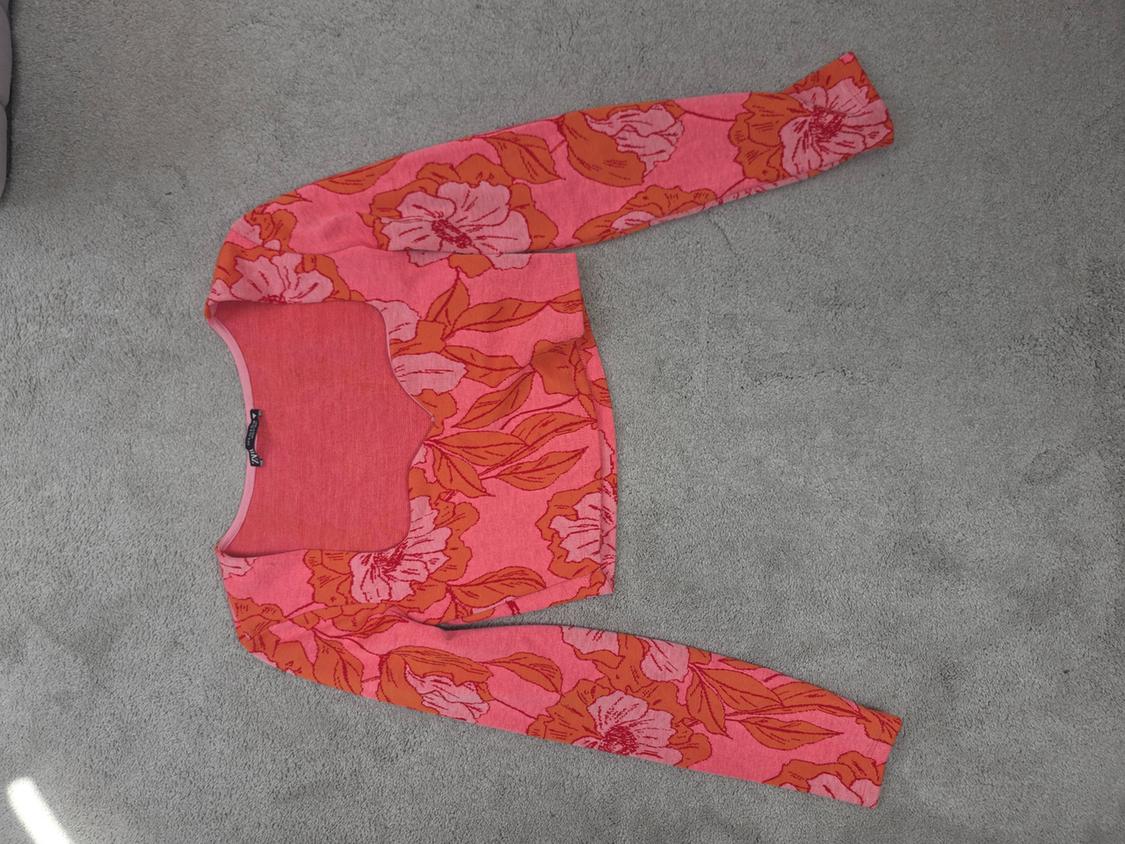 Pink jumper with orange and pink floral print, long-sleeved, on a grey rug.
