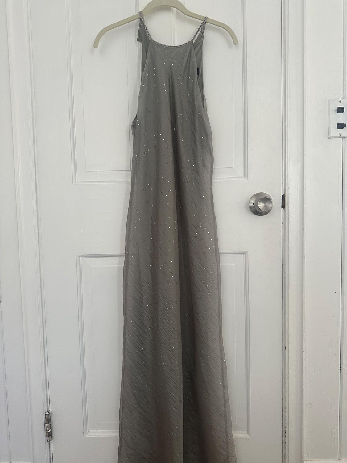 Long gray dress with shimmering details hanging on a hanger over a white door.