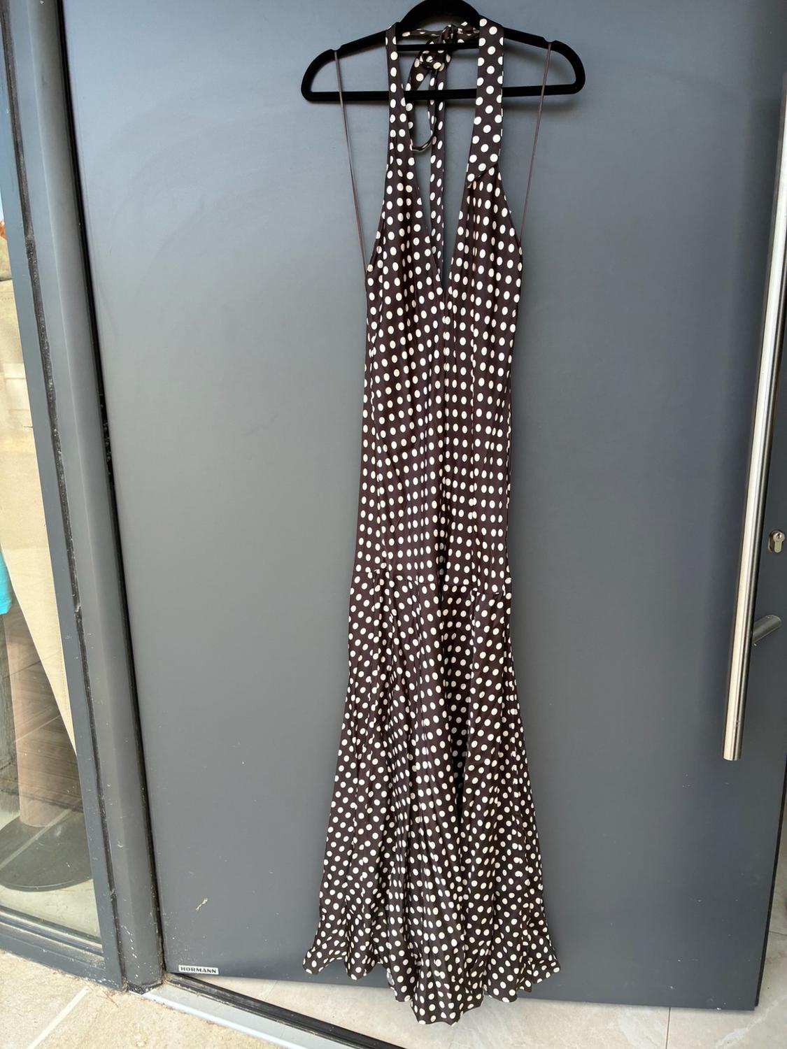 Long dark brown dress with white polka dots and a halter neck, hanging on a grey door. Visible text: HORMANN.