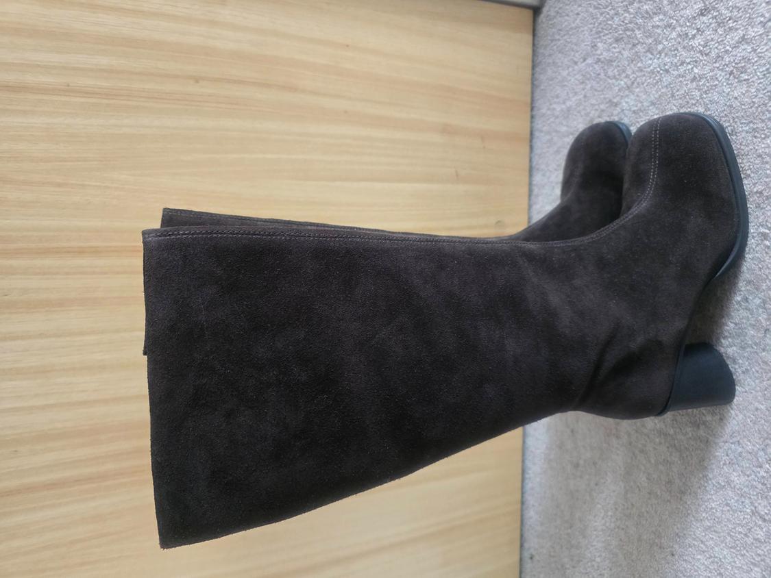 Dark brown suede knee-high boots with a chunky heel, resting on a light wooden surface and a beige rug.