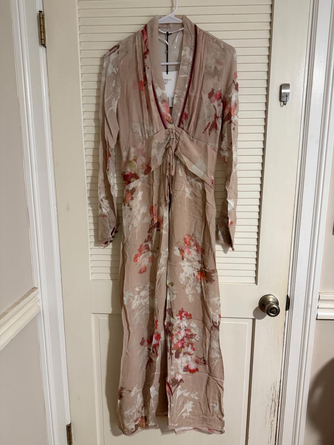 Long beige chiffon dress with a floral print in red and white tones, hanging on a white door with a metallic knob.