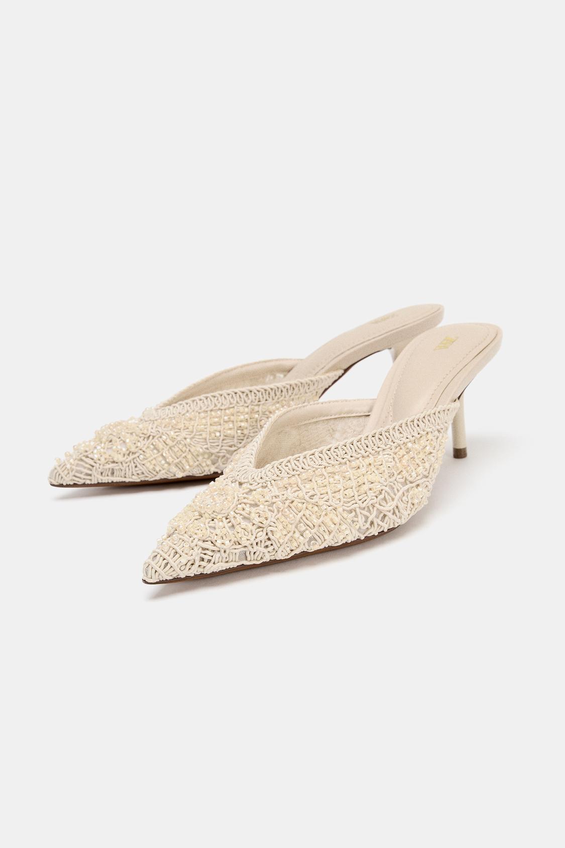 Beige high-heeled shoes with a pointed toe and detailed embroidered design on the upper.