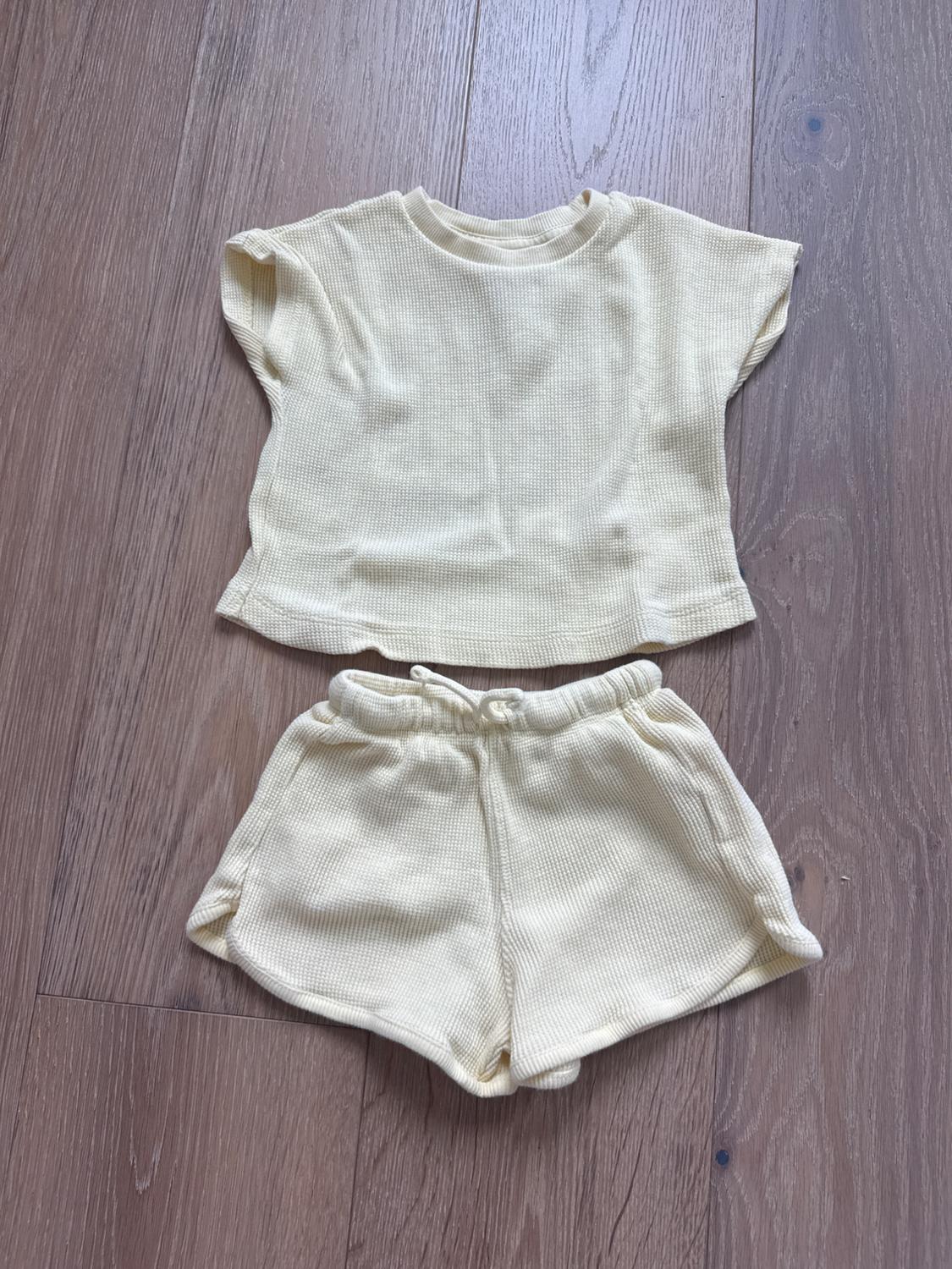 Light yellow children's set on a wooden floor, consisting of a short-sleeved T-shirt and drawstring shorts.