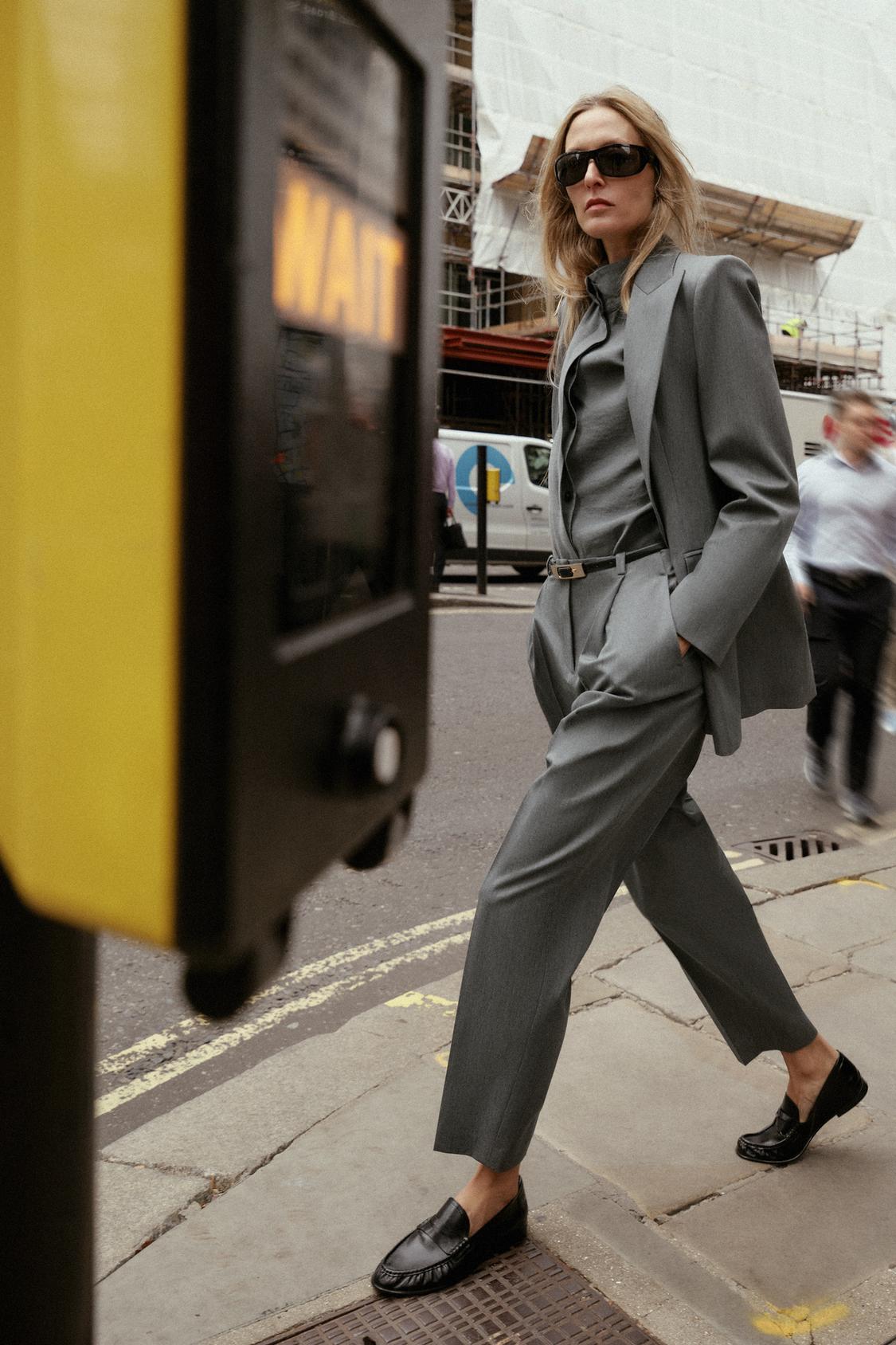 Siva obleka s suknjičem z reverji, hlačami s kripom in pasom. Vidni stranski žepi.