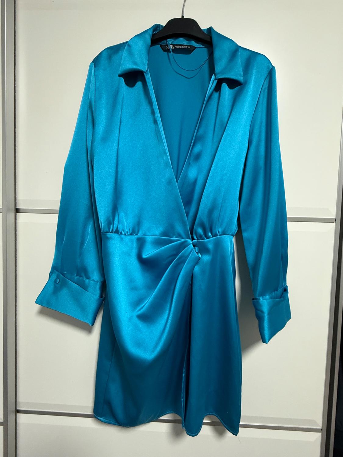 Satin blue dress with a collar and long sleeves, hanging on a black hanger against a white background.