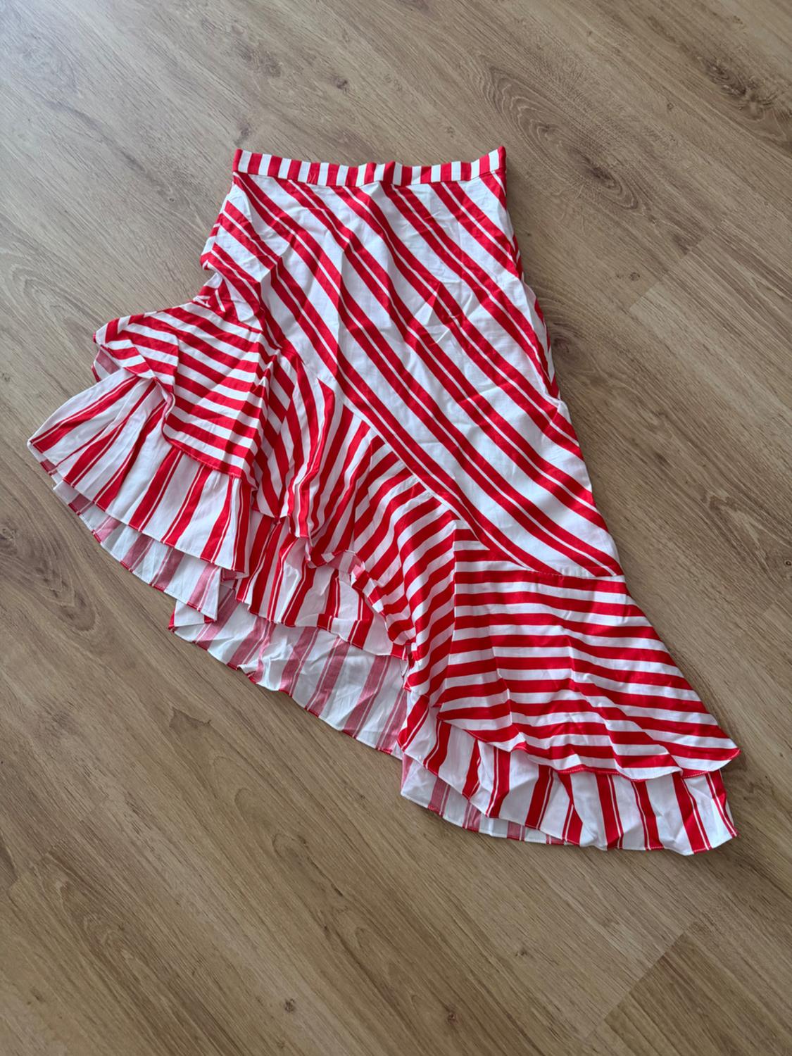 Red and white striped asymmetrical skirt with ruffles, laid out on a light wood floor. Casual and relaxed style.