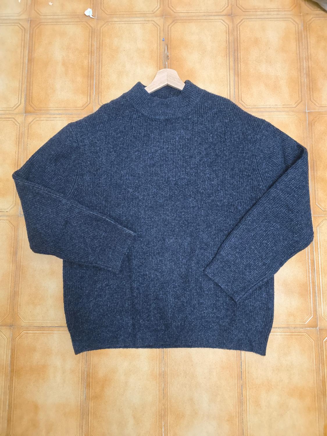 Dark grey chunky knit roll neck jumper, laid out on a brown tiled background.