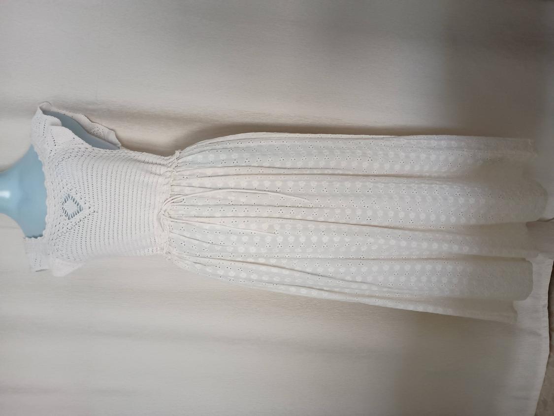 White lace dress on a light blue mannequin, with a knitted design on the top and a skirt with floral embroidery.