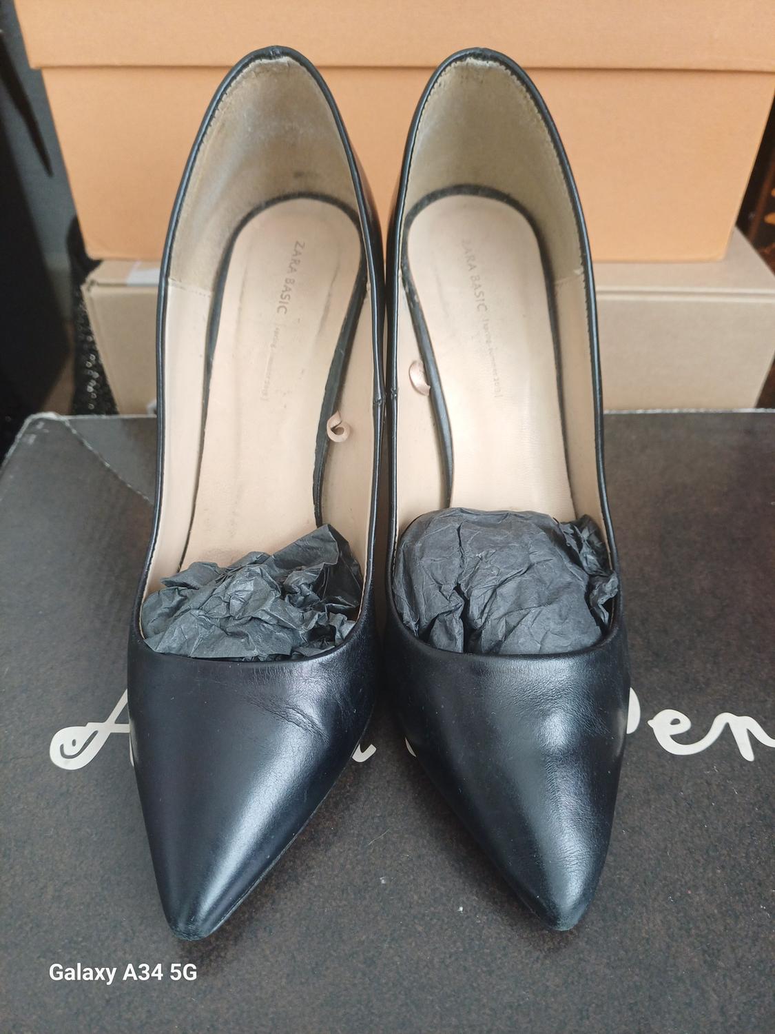 Front view of black stiletto heels with pointed toe and paper stuffing, on a box with the text 'Galaxy A34 5G'.