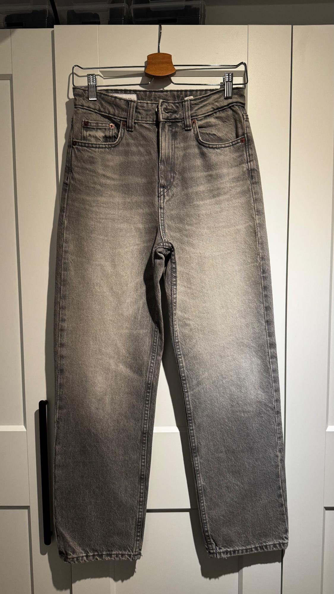 Grey jeans hanging on a wooden hanger over a white door. Worn style and straight cut.