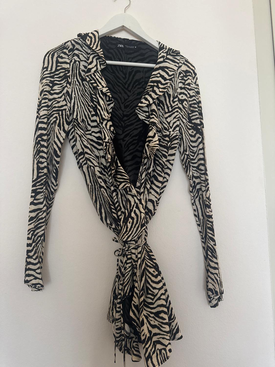 Black and white zebra print long-sleeved dress, hung on a white hanger against a white wall.