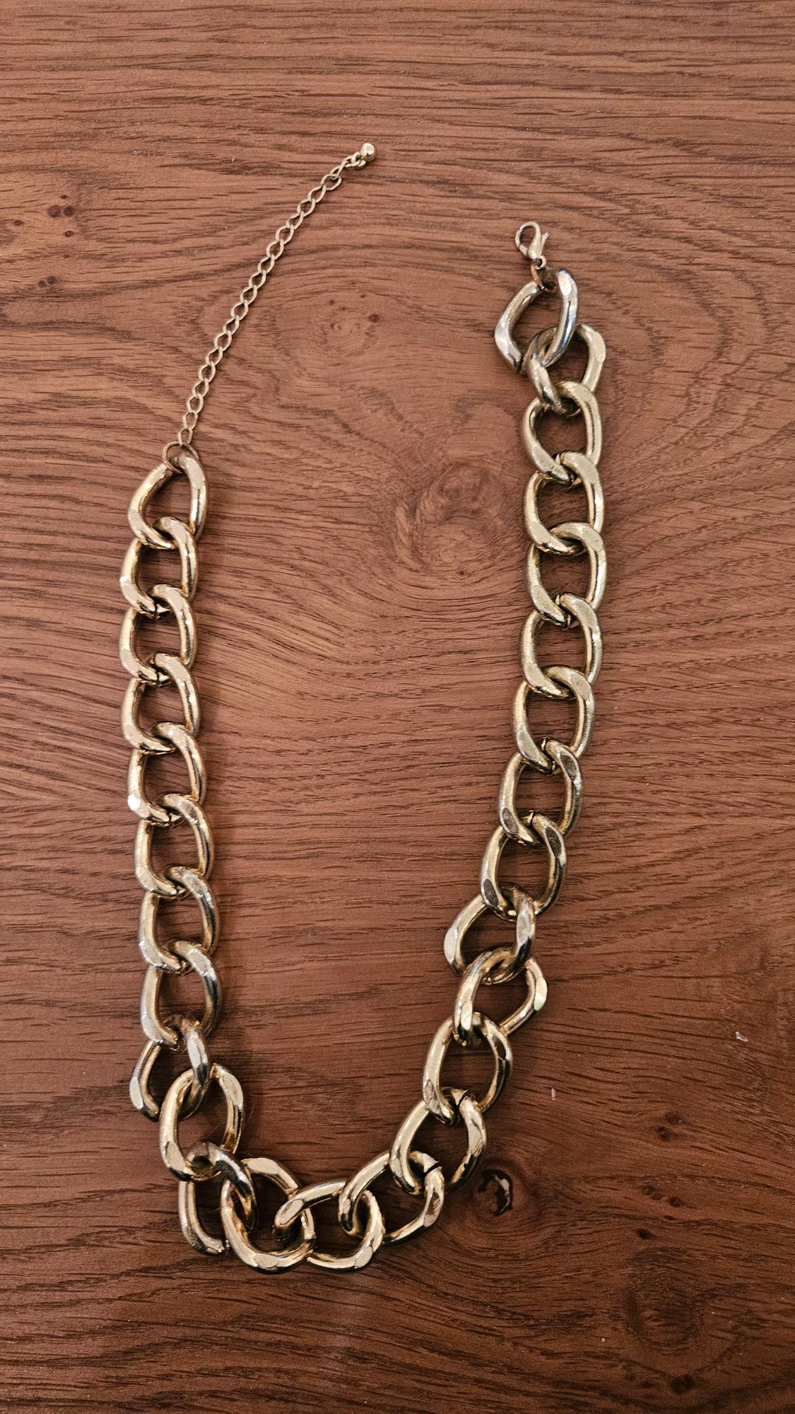 Thick gold chain on a brown wooden surface. The chain has a hook clasp and an adjustable extender.