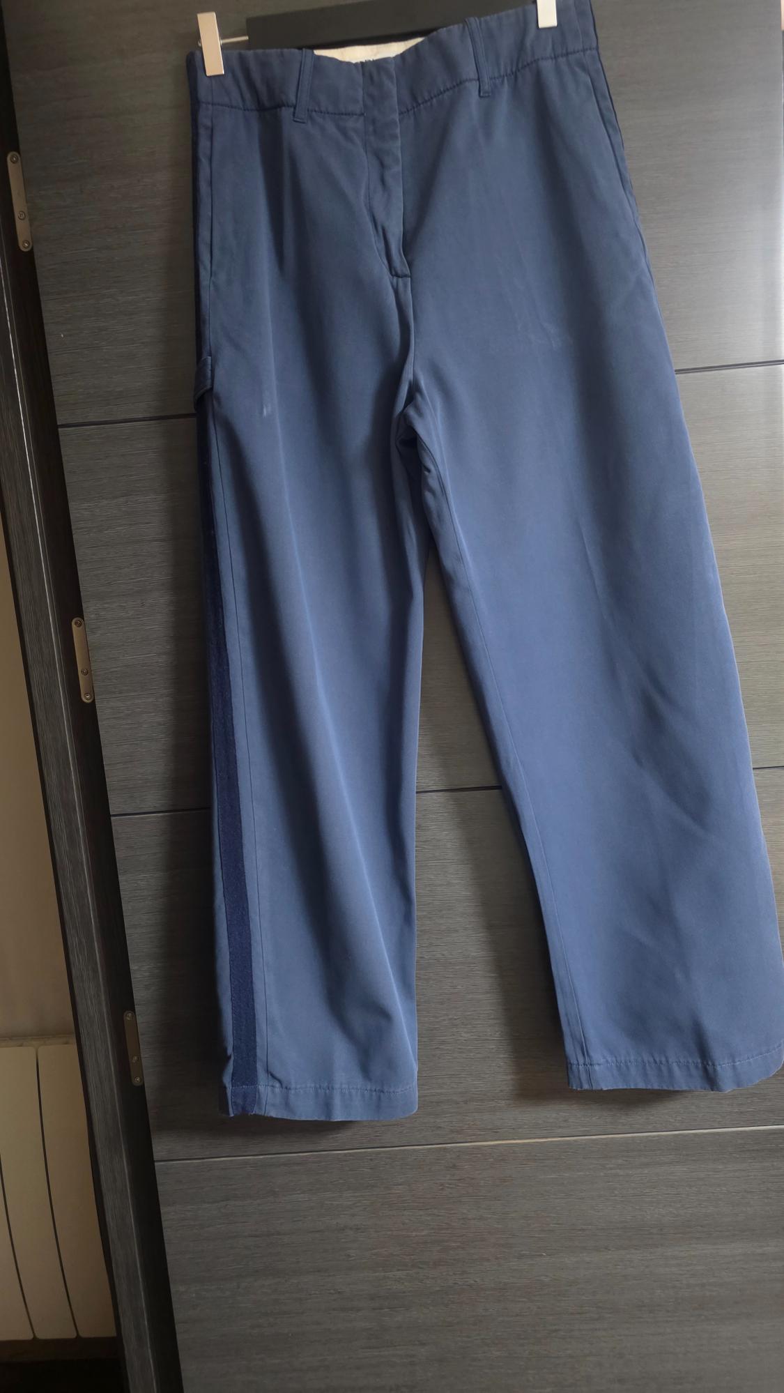 Casual blue trousers with a dark side stripe, hanging on a grey wooden door in a relaxed, homely setting.