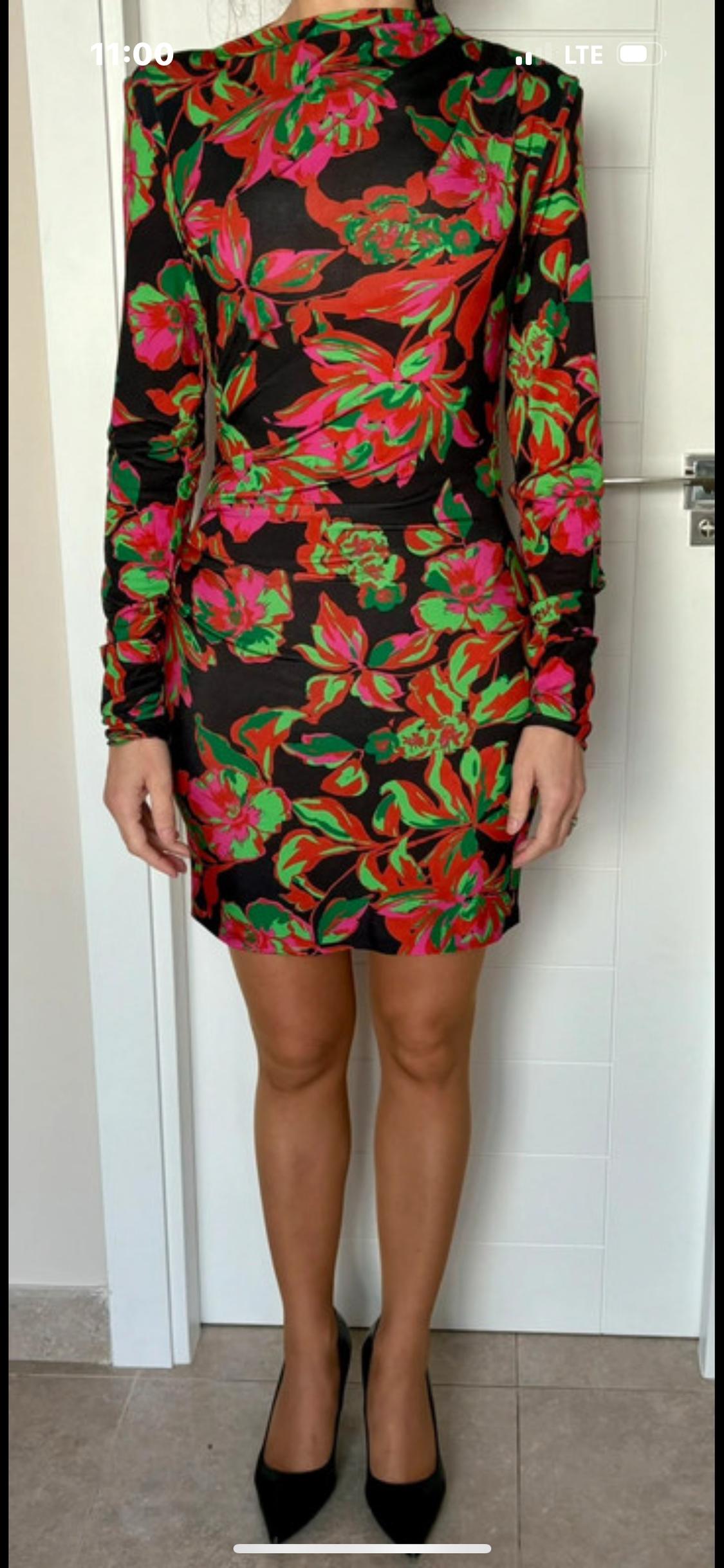 Model in a long-sleeved, form-fitting dress with a floral print in red, green, and pink on a black background, and black heels.
