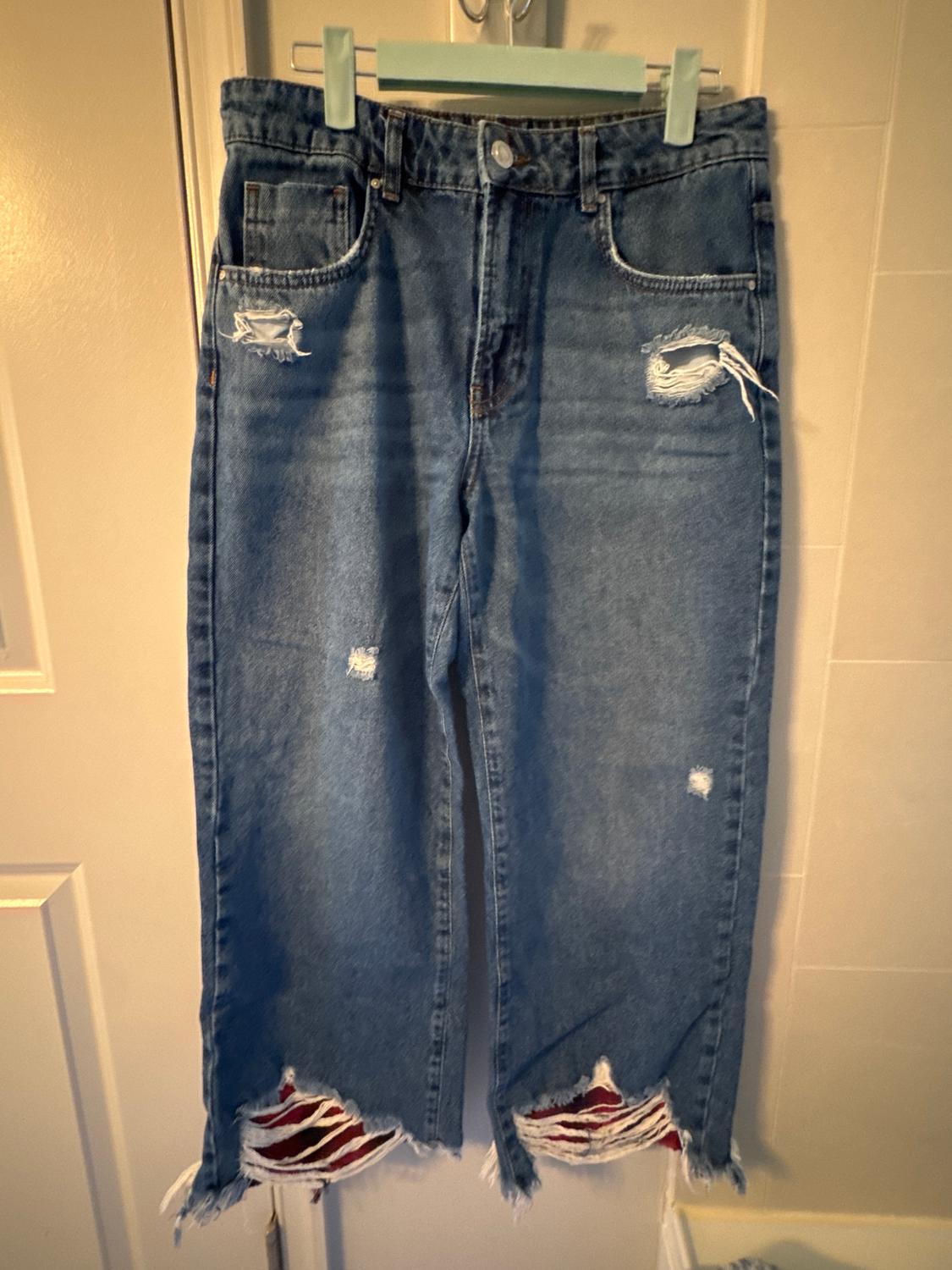 Distressed blue jeans hanging on a hanger, with rips at the knees and a frayed hem.
