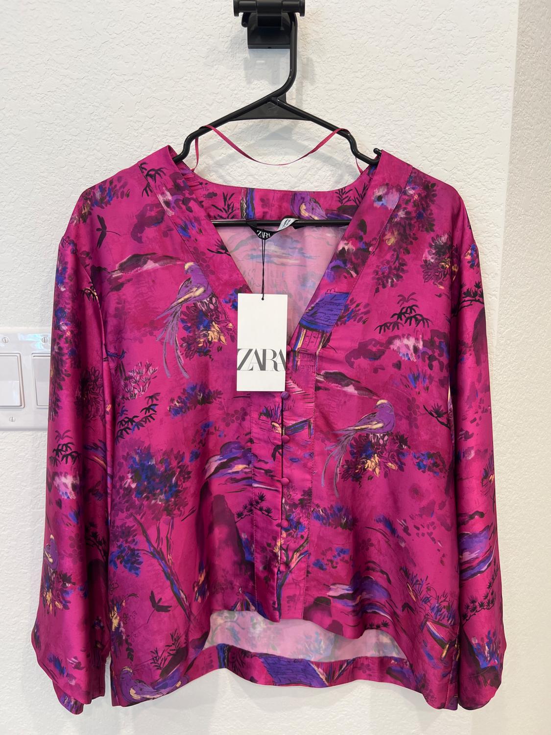 Fuchsia blouse with floral and bird print, hanging on a black hanger. Zara tag visible in the center.