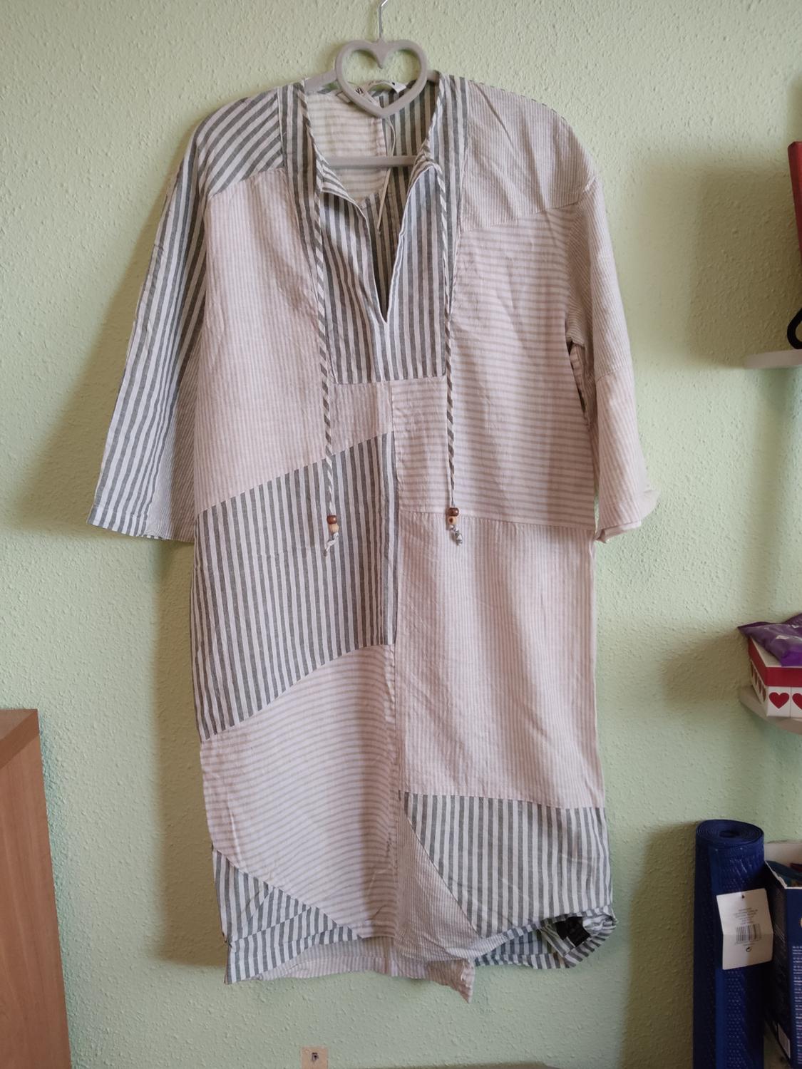 Casual grey and white striped panelled tunic dress with drawstrings, hanging on a heart-shaped hanger against a light green wall.