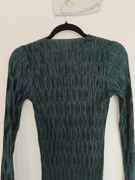 Dark green pleated long-sleeved dress hanging on a black hanger against a white background.