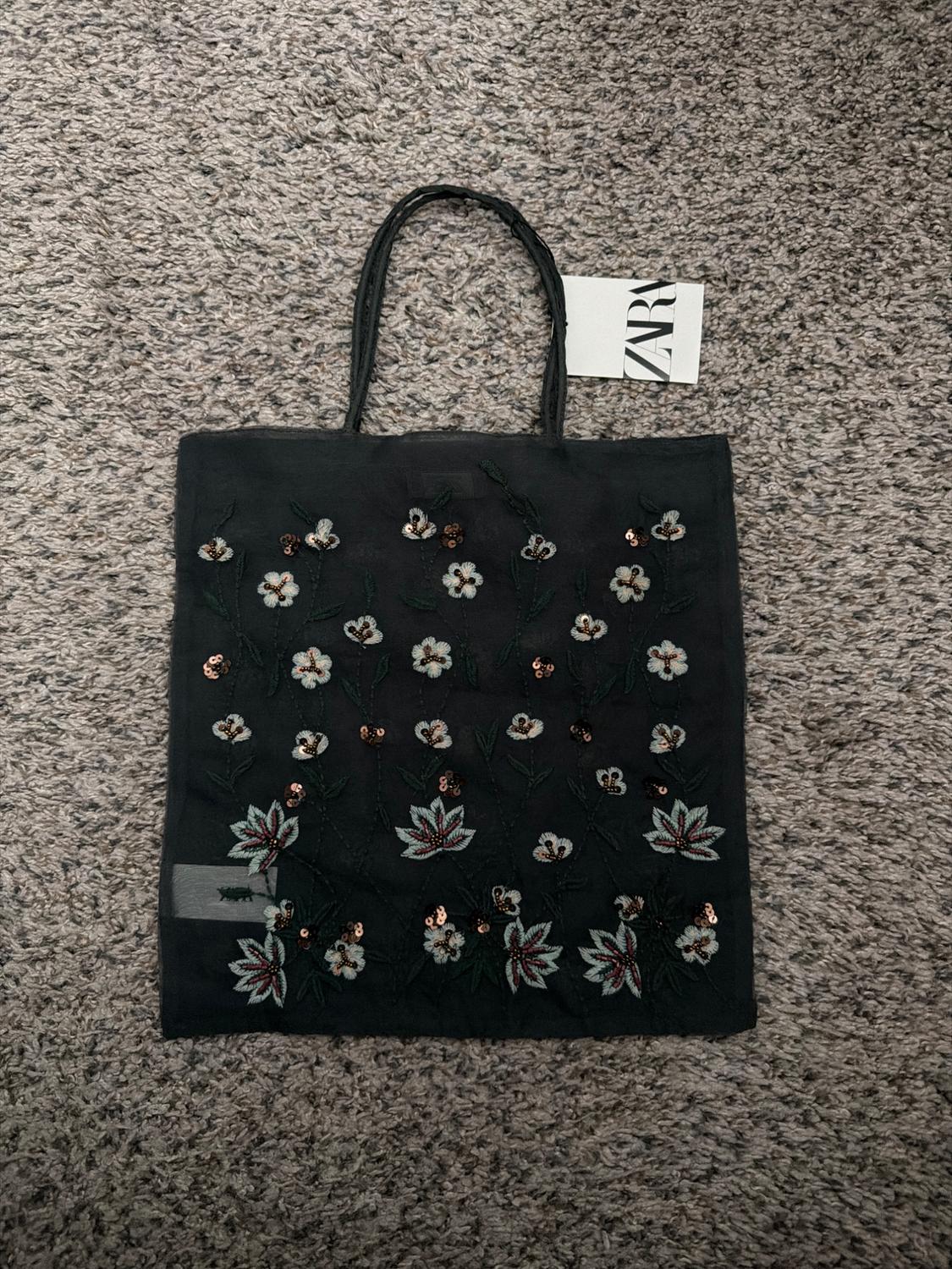 Black handbag with floral embroidery and sequins, on a grey rug. Visible label with text "ZARA".