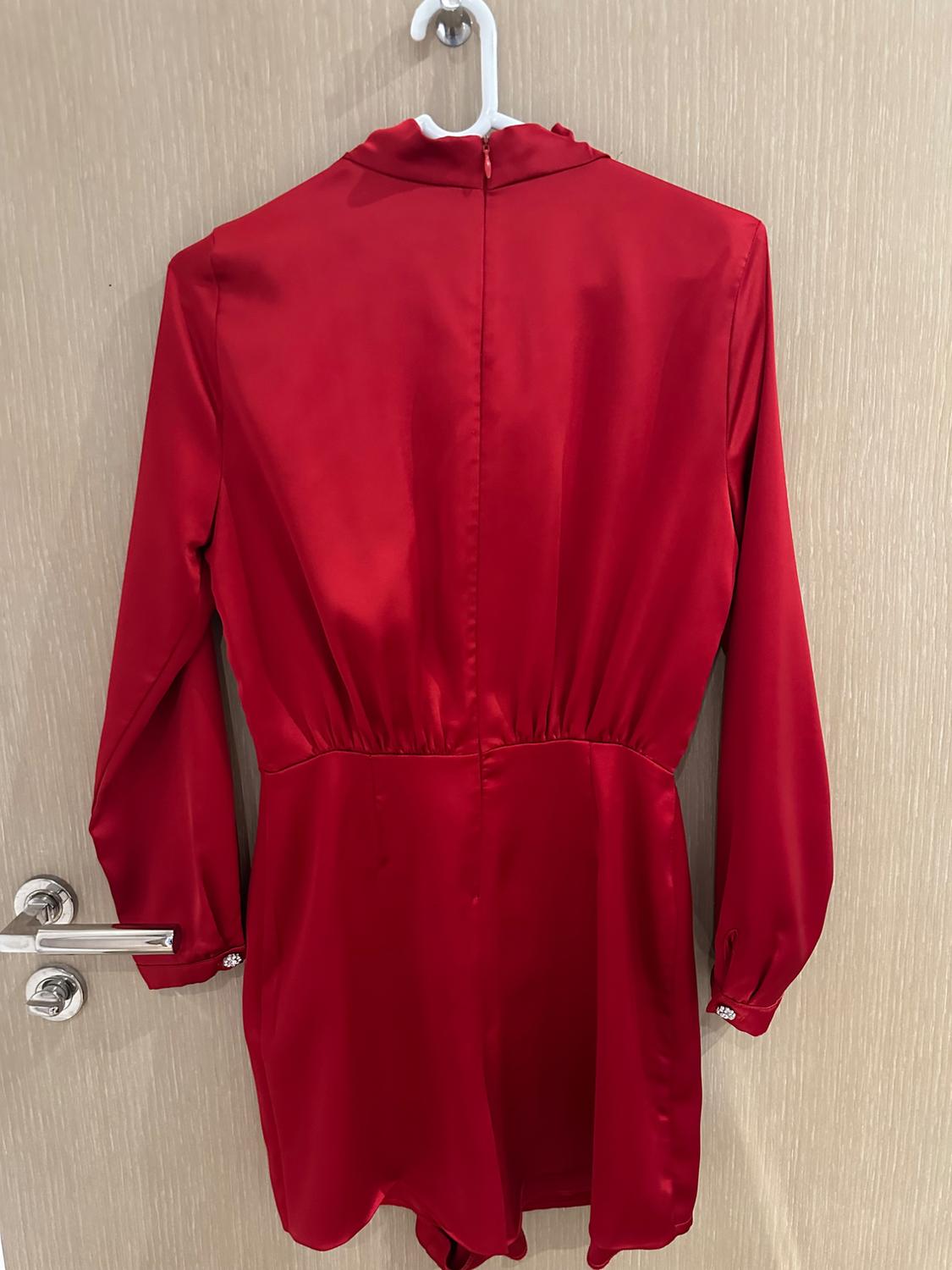 Rear view of a red satin jumpsuit with long sleeves and a high neck, hanging on a white hanger on a light wood door.