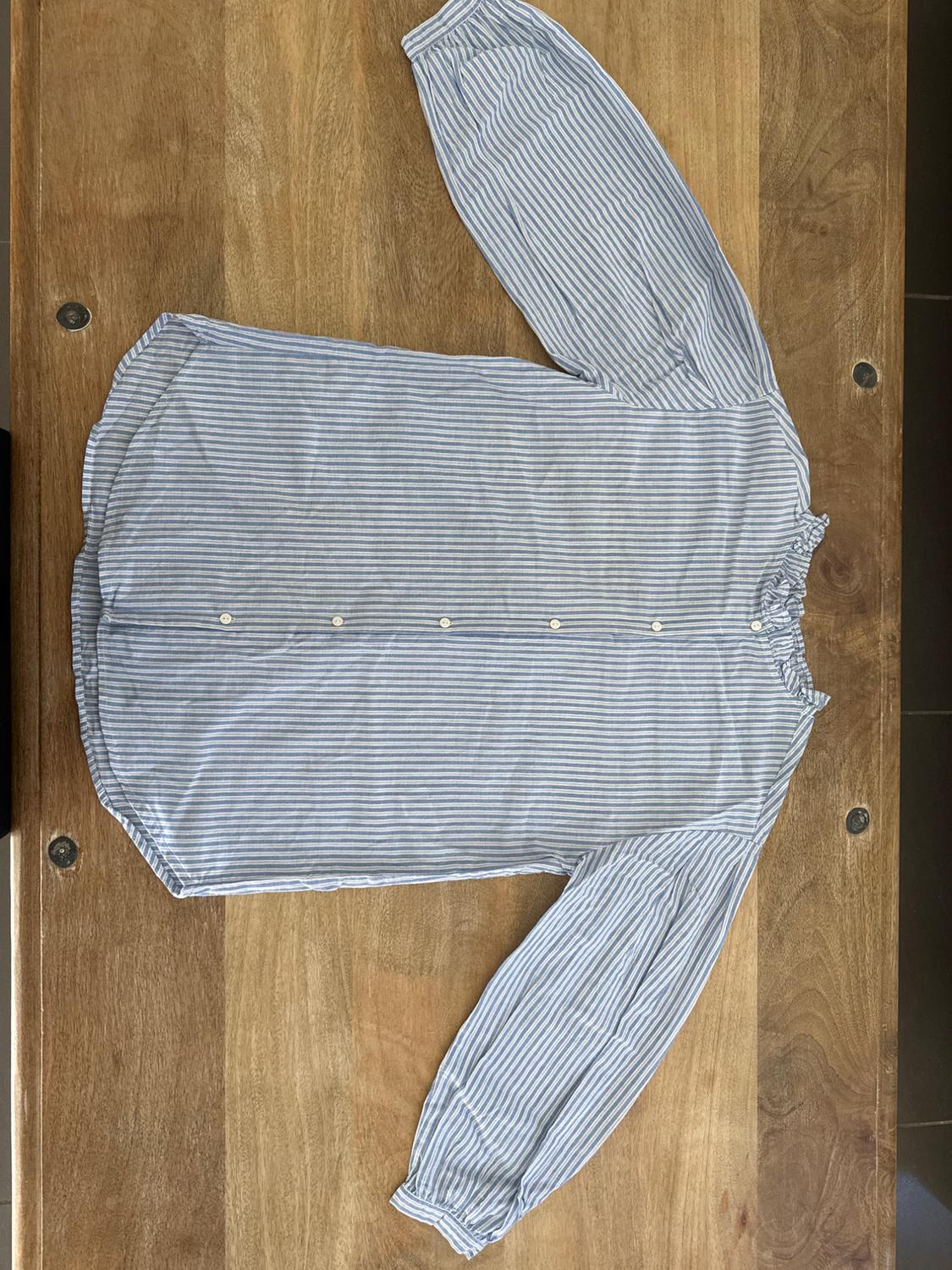 Blue and white striped button-up shirt, long-sleeved with a gathered collar, placed on a wooden table.