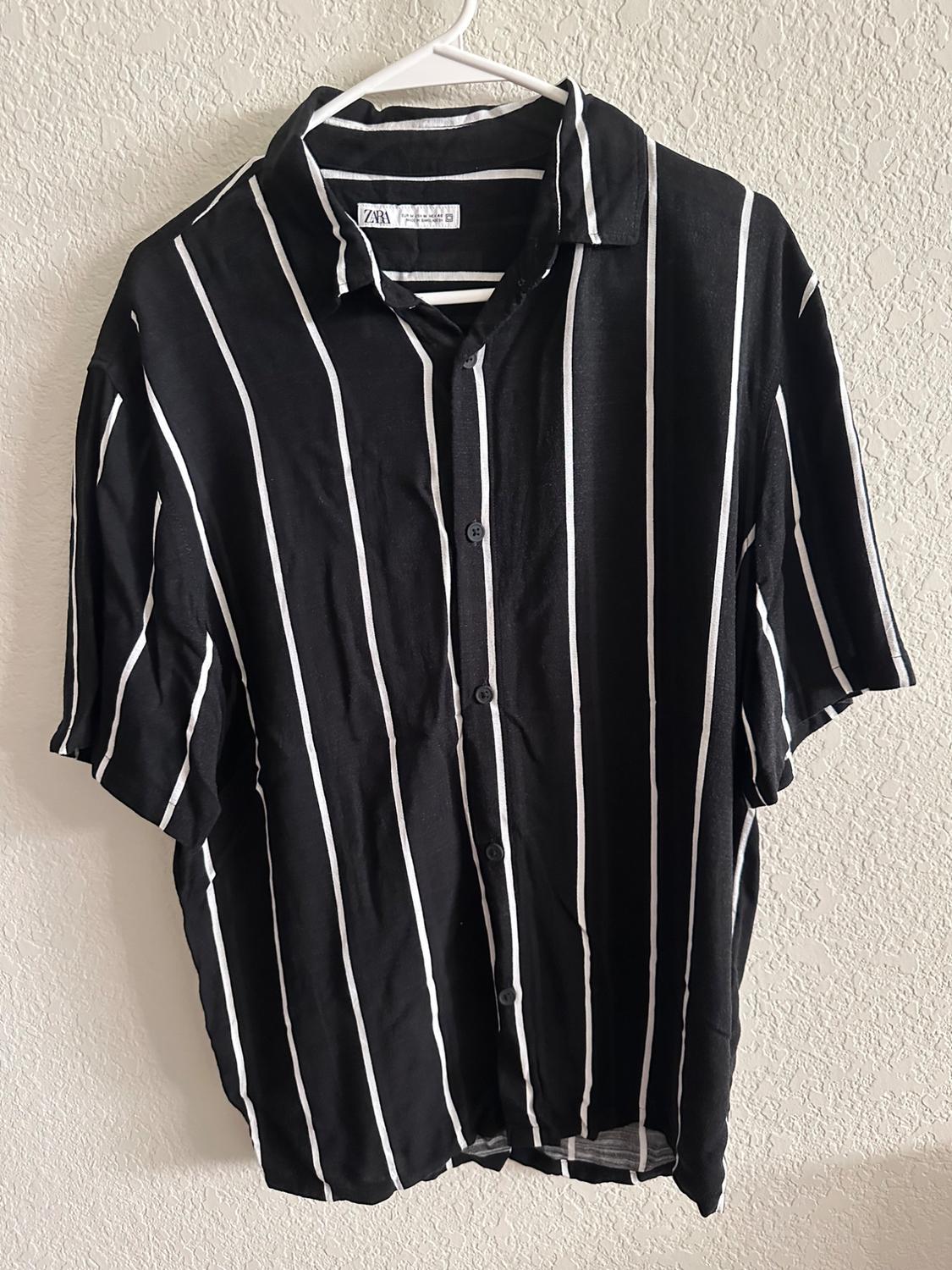 Black shirt with white vertical stripes hanging on a white hanger, with a visible label that says "Zara".