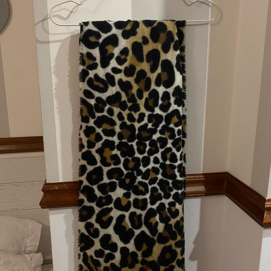 Leopard print fabric in brown and black tones, hanging on a white hanger against a white wall with wooden moulding.