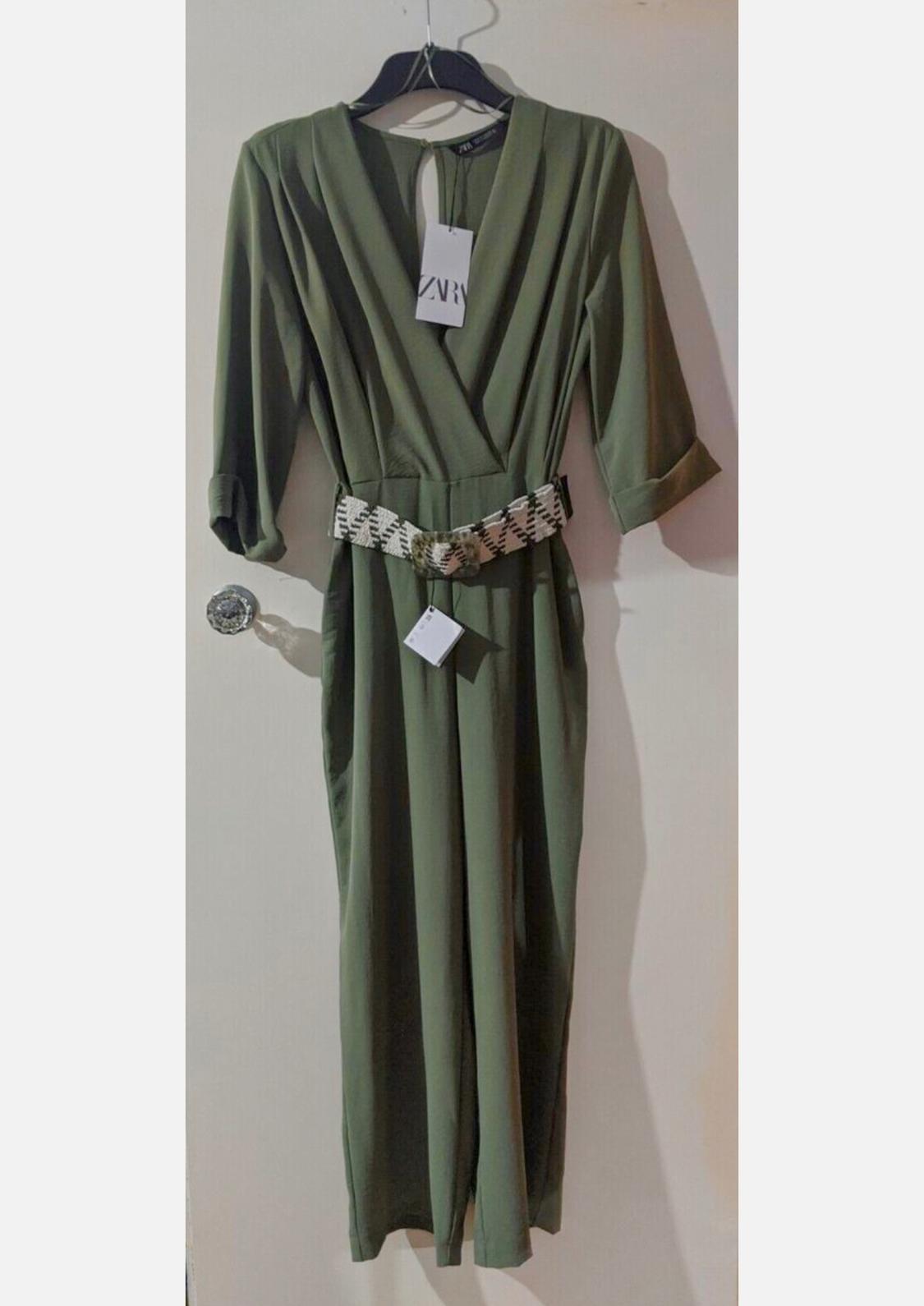 Front view of a green jumpsuit with a black and white patterned belt, three-quarter sleeves and a V-neck.
