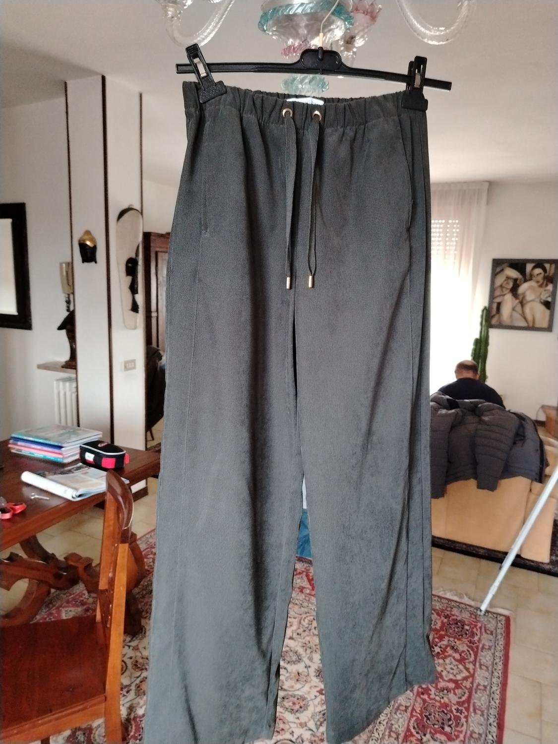 Grey trousers hanging on a hanger in a living room, with wooden furniture and a decorative rug in the background.
