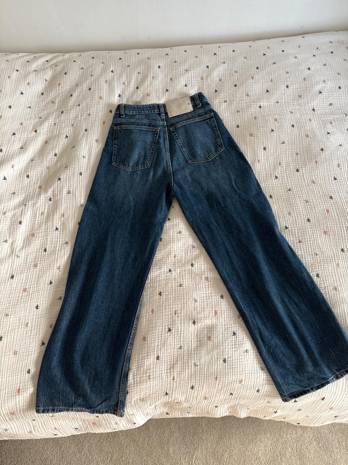 Dark blue denim jeans placed on a white bedspread with small colourful patterns.