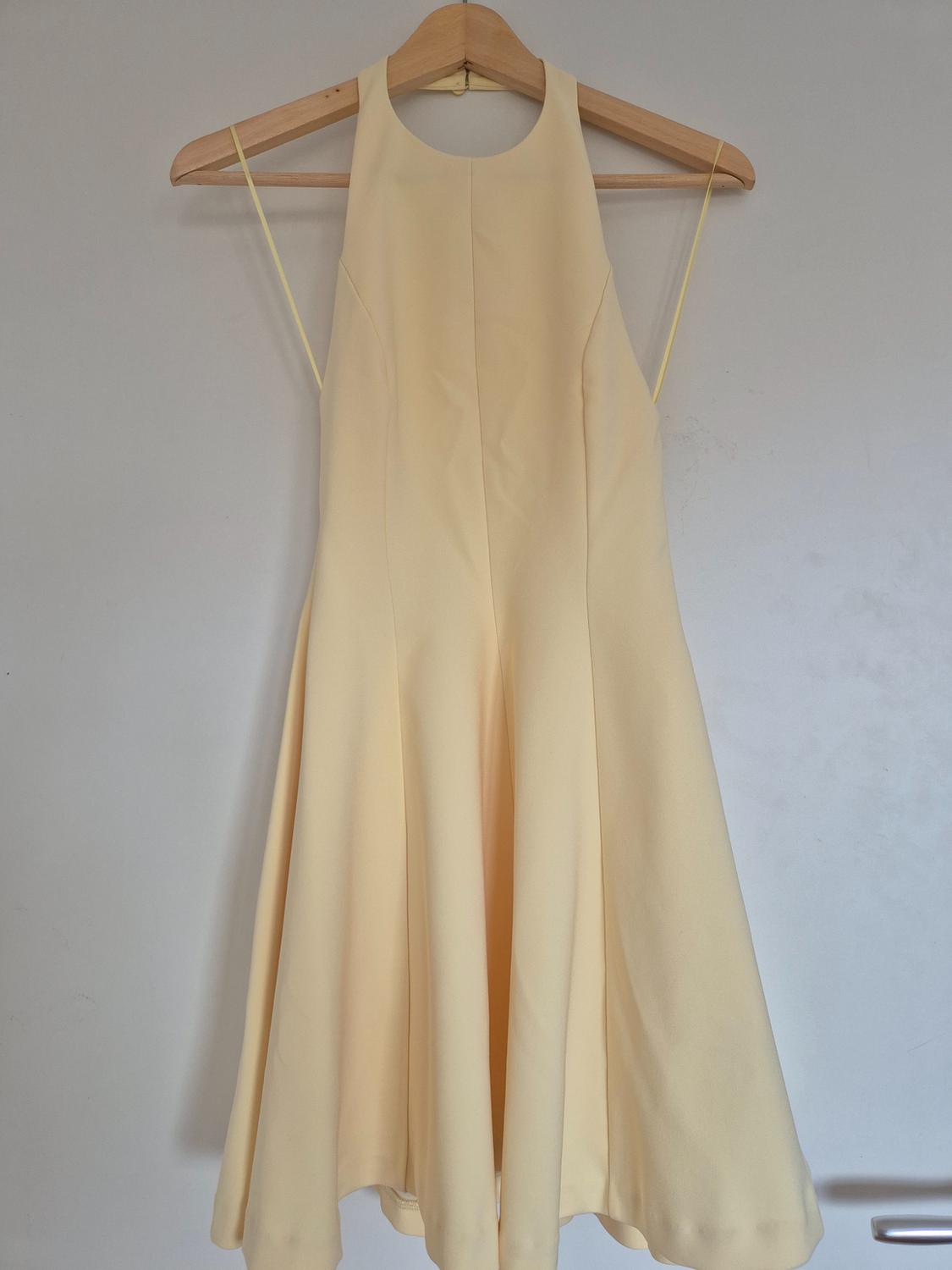 Light yellow sleeveless dress hanging on a wooden hanger against a white background.
