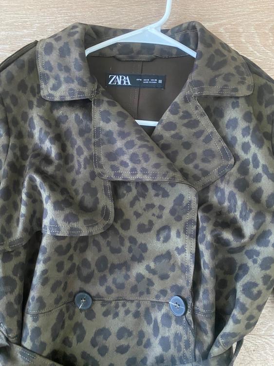 Leopard print coat in brown and black tones, hanging on a white hanger. Visible tag: "ZARA".