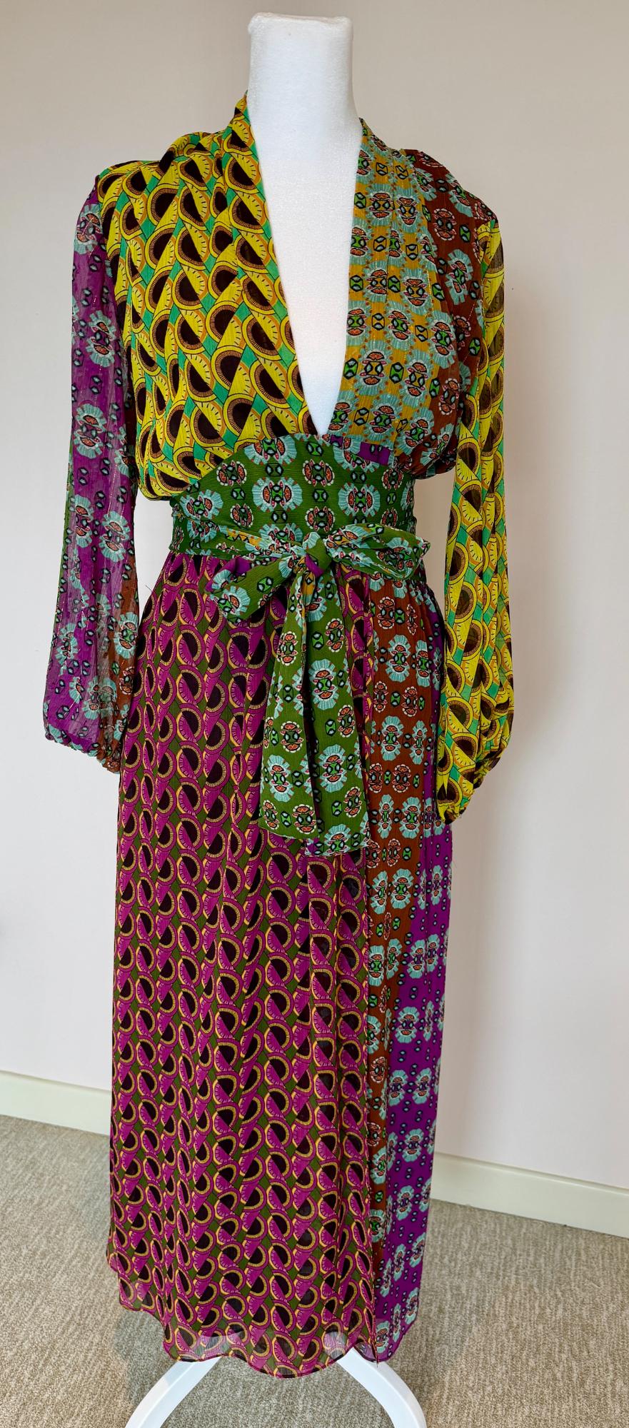 Long dress on a mannequin with a multicolored geometric print in shades of green, yellow, purple, and brown, with a matching belt.
