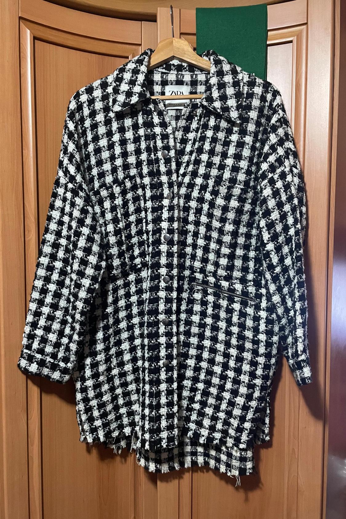 Front view of a jacket in a black and white pattern with side pockets and metal buttons.