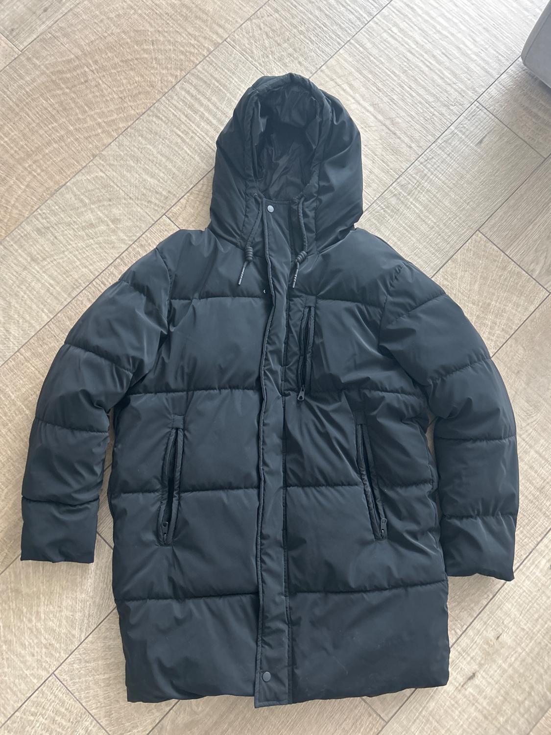 Black padded coat with a hood and zip fastening, laid on a light wooden floor.