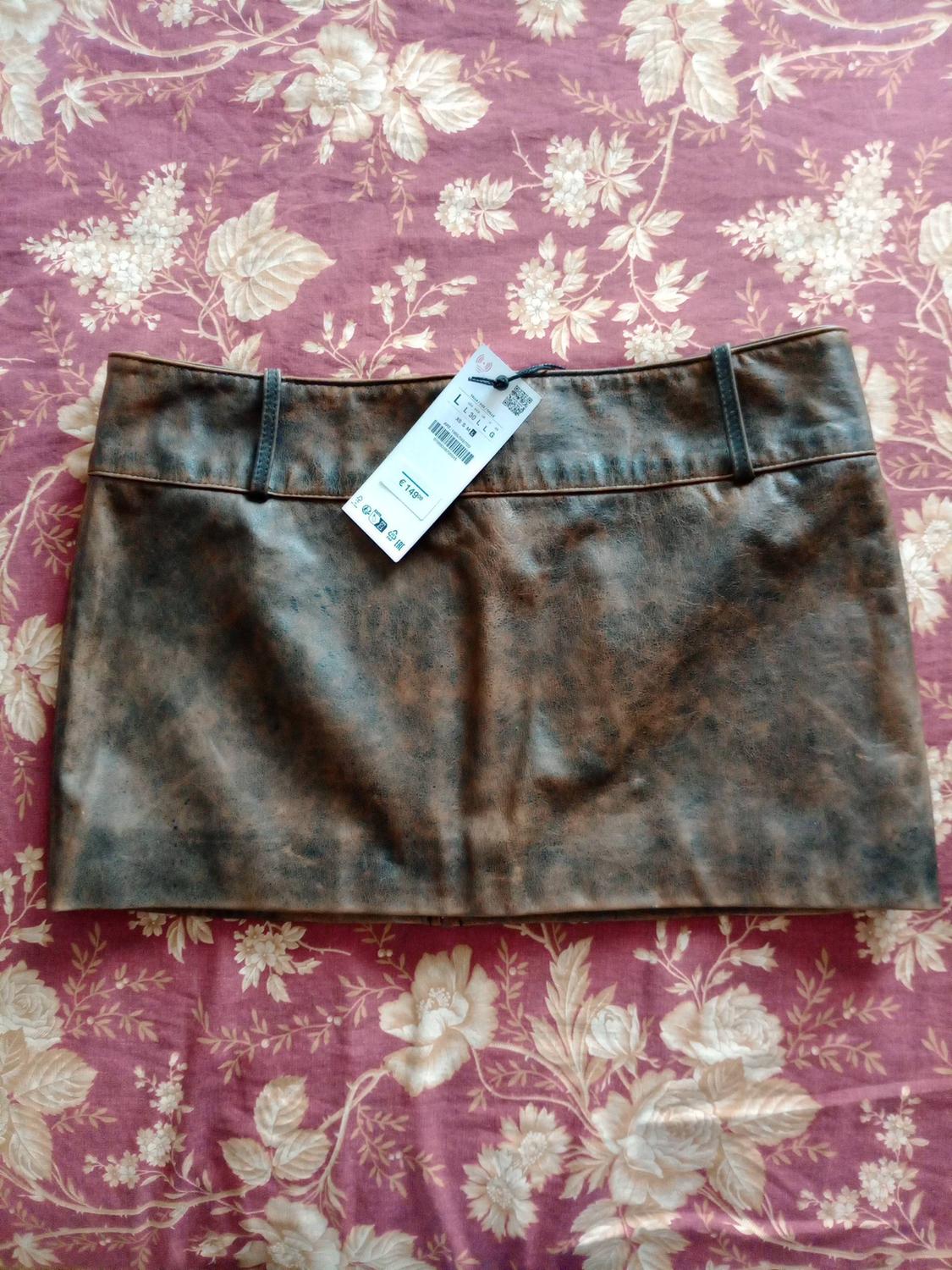 Distressed brown mini skirt with belt loops and a label bearing the text "L" and "€ 149", set against a burgundy floral print fabric background.