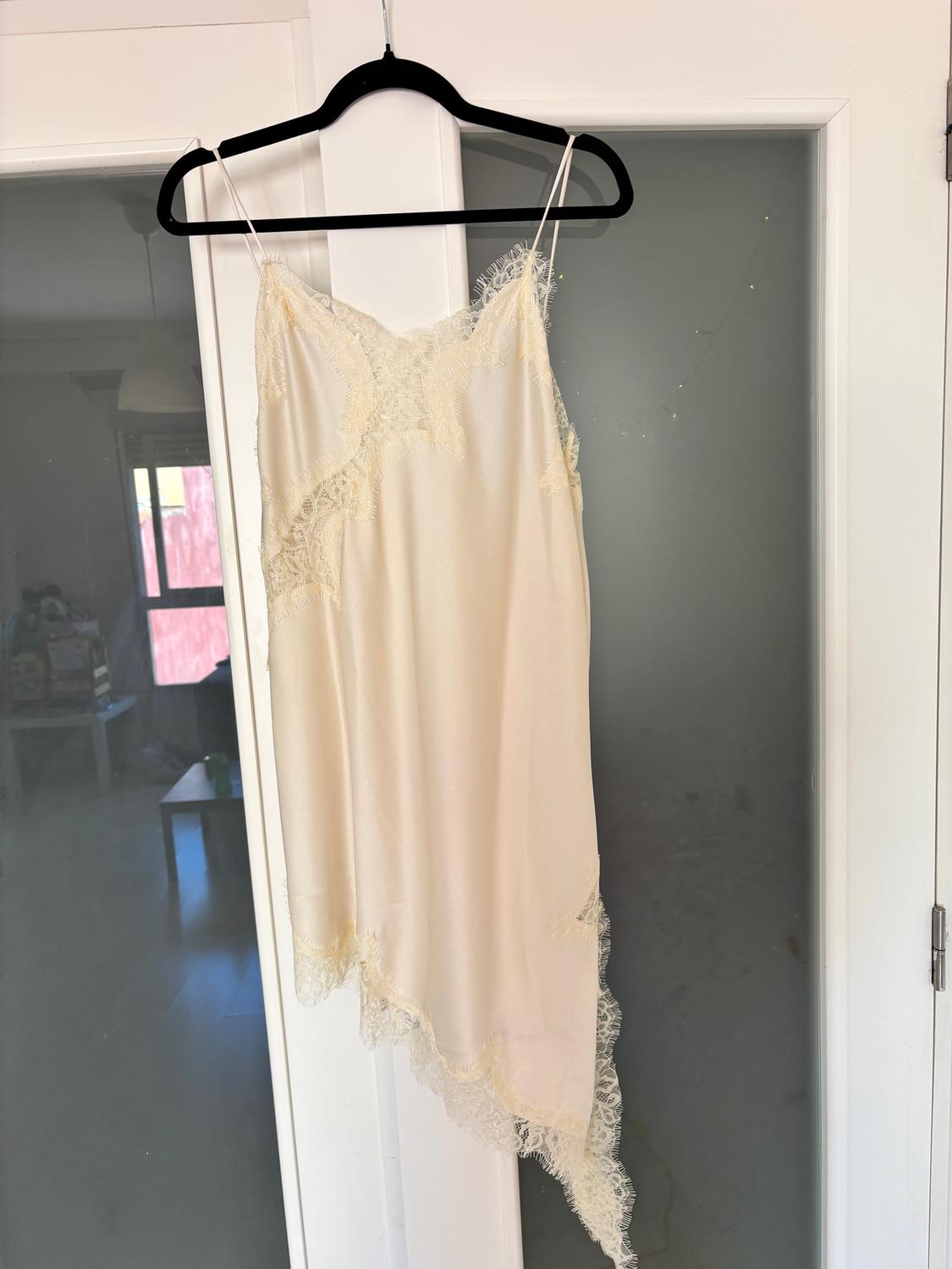 Cream-coloured strappy dress with lace hanging on a black hanger in front of a frosted glass door.