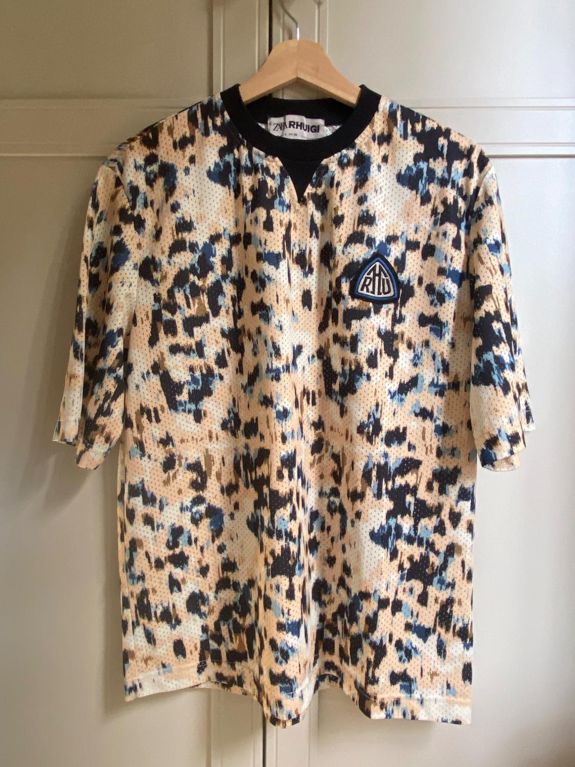 T-shirt with an abstract print in beige, blue, and black tones. "RH" logo on the chest. "RH Rhuigi" label on the collar.